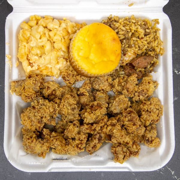 A soul food takeout container with fried chicken, macaroni and cheese, rice, and a cornbread muffin.