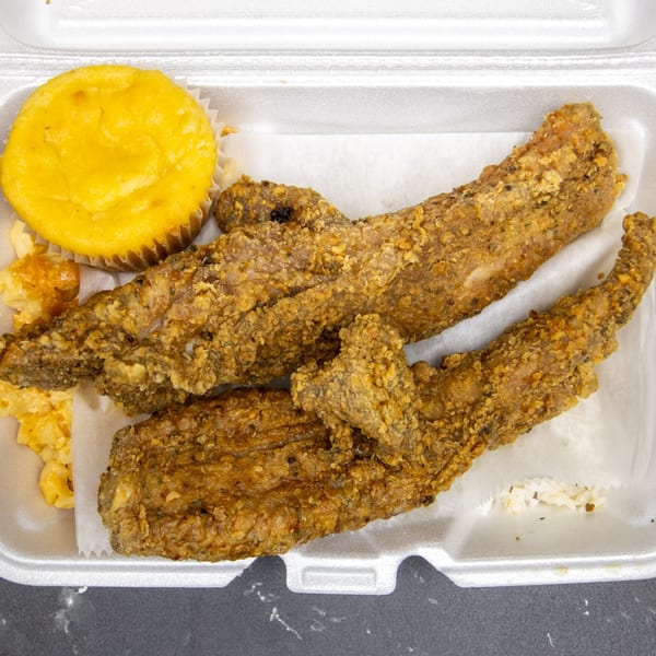 Fried fish, macaroni and cheese, and a cornbread muffin in a styrofoam takeout container.