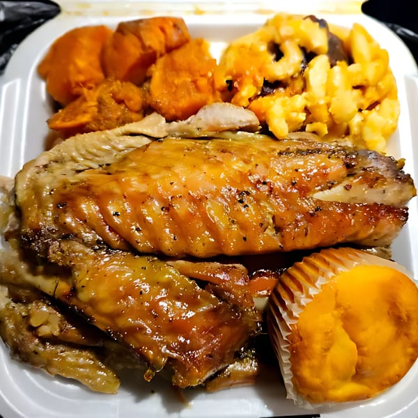 Soul food meal with glazed chicken, candied yams, macaroni and cheese, and a cornbread muffin.